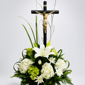 Tributo de Serenidad elegante arreglo fúnebre elaborado con lirios y hortensias, acompañado de helecho cuero, liriope y un Cristo sobre una base de bejuco. Una composición sobria para expresar respeto, condolencias y acompañamiento.