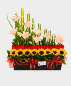 Sol de Amor es legre y elegante arreglo floral elaborado con girasoles, rosas y lirios, acompañado de liriope, rusco y hoja de lino sobre una base de madera. Un detalle perfecto para celebrar y sorprender.