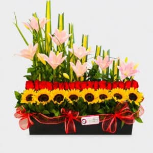 Sol de Amor es legre y elegante arreglo floral elaborado con girasoles, rosas y lirios, acompañado de liriope, rusco y hoja de lino sobre una base de madera. Un detalle perfecto para celebrar y sorprender.